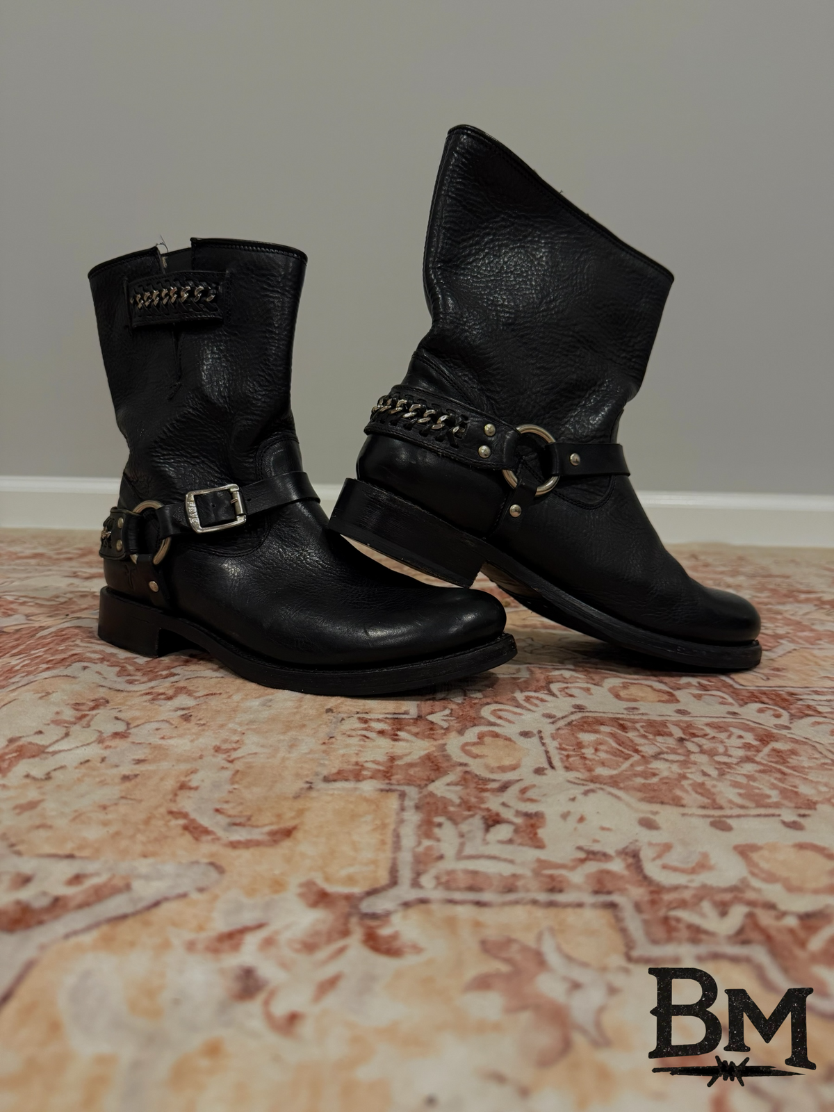 Barnwood Manor black leather mid-calf motorcycle boots with harness straps, metal hardware, and chain detail.